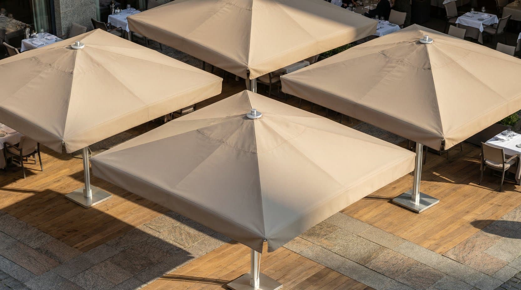 Vier große quadratische Gastro-Sonnenschirme auf einer Terrasse, Schattenkante auf Holz und Stein